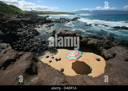 Hell farbige Sonnenschirm In einem Sandy-Kreis umgeben von Lavafelsen direkt am Meer. Stockfoto