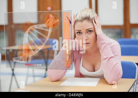 Blonde Frau denken schwer während des Studiums auf Schnittstelle mit DNA Stockfoto