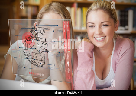 Zwei lächelnde Studenten auf der Suche auf Laptop und futuristische Interface mit Herz-Diagramm Stockfoto