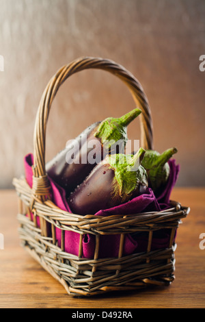 Rohe Auberginen oder Auberginen im Korb auf hölzernen Backround. Stockfoto