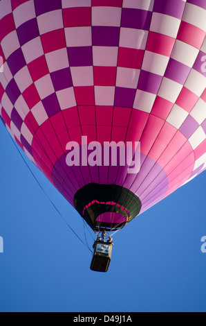 Ein fröhliche rosa und lila überprüft Heißluftballon steigt in einem klaren blauen Himmel. Stockfoto