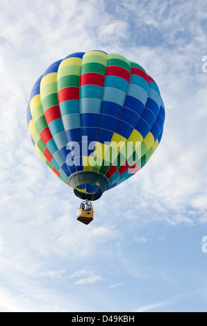 Ein regenbogenfarbenen Heißluftballon schwebt durch weiße Wolken am blauen Himmel. Stockfoto