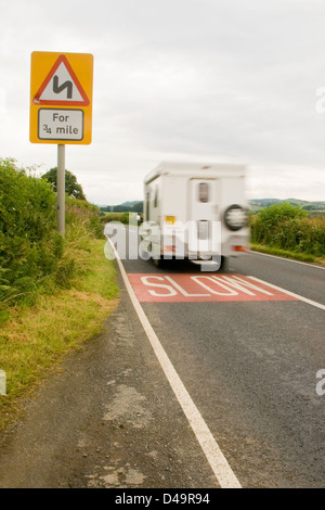 Einen Campervan Reisen entlang eine britische Landschaft Straße vorbei an einer Slow unterzeichnen auf der Straße. Stockfoto