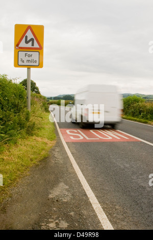 Ein weißer Lieferwagen vorbei an einem langsamen Schild auf einer ländlichen Landstraße in der englischen Landschaft zu beschleunigen. Stockfoto