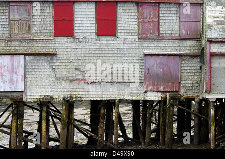 Rote Fensterläden auf einem verfallenen grau-Schindeln Lager thront auf alten Log-Pfähle in Lubec Maine. Stockfoto