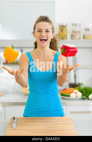 Glückliche junge Frau Jonglieren mit Paprika in Küche Stockfoto