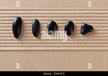 Fünf schwarze Kieselsteine auf einen geharkt Sand Zen-Garten. Stockfoto