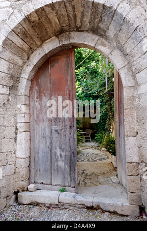 Rhodos. Griechenland. Malerischer Blick auf ein altes steinernes Gebäude mit einem Rundbogen eröffnet, die in einem inneren Garten im Innenhof. Stockfoto