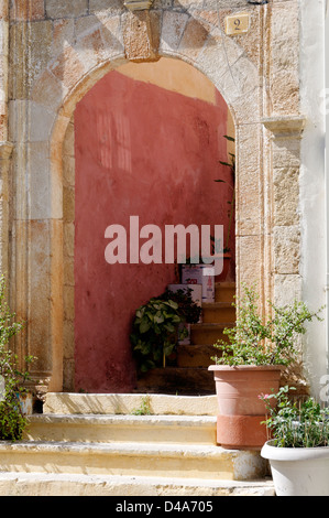 Rhodos. Griechenland. Rosa Gebäude aus Stein mit gewölbten Stein Eingang von Topf Pflanzen Blumen in Rhodos Altstadt gesäumt. Stockfoto