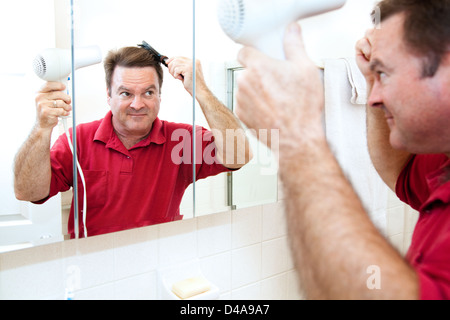Man trocknet seine Haare mit einem Hand-held-Föhn im Badezimmerspiegel. Stockfoto