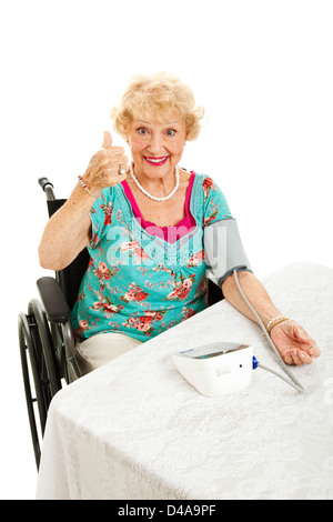 Ziemlich senior Frau im Rollstuhl nehmen ihr Blutdruck und geben Daumen hoch Zeichen. Isoliert auf weiss. Stockfoto