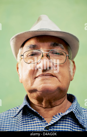 Menschen und Emotionen, Porträt von Ernst senior hispanic Mann mit Brille und Hut Blick in die Kamera vor grünem Hintergrund Stockfoto