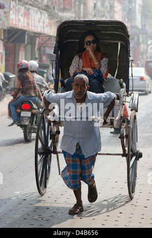 Eine Rikscha-Puller transportiert eine Frau In Kolkata, Indien Stockfoto