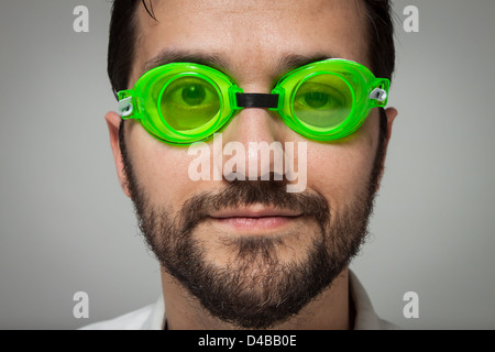 Porträt eines jungen bärtigen Mannes mit grünen Gläsern auf grauem Hintergrund schwimmen Stockfoto