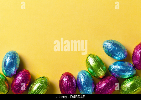 Ostern-Hintergrund mit bunten Schokoladeneier auf gelbem Papier. Ansicht von oben, Makroaufnahme Stockfoto