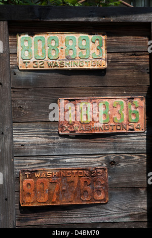 Drei rostige Nummernschilder hängt an einer Holzwand in Ashford, Washington, USA Stockfoto