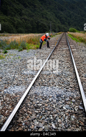 Ein Mann mit Warnschutz Jacke und Schutzhelm mit einem Vorschlaghammer arbeiten an einer eingleisigen Eisenbahnstrecke. Stockfoto