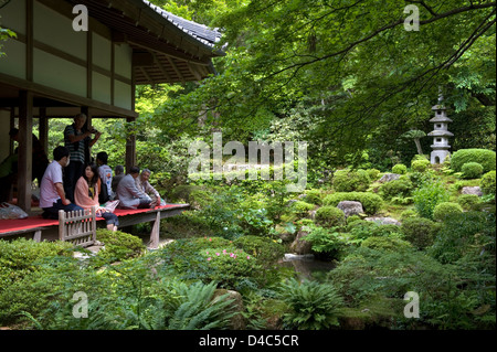 Besucher genießen den Blick auf eine üppige grüne japanische Landschaftsgarten von der Veranda im Sanzenin Tempel in Ohara, Kyoto, Japan. Stockfoto