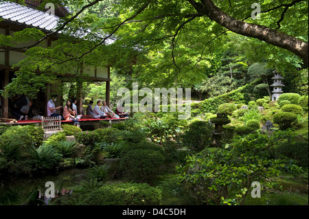 Besucher genießen den Blick auf eine üppige grüne japanische Landschaftsgarten von der Veranda im Sanzenin Tempel in Ohara, Kyoto, Japan. Stockfoto