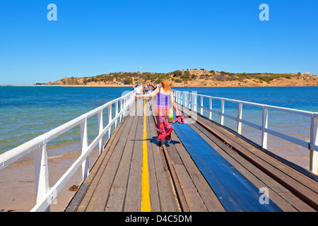 Bunt gekleidete Frau zu Fuß entlang einer Straßenbahn Spur auf dem Damm zwischen Victor Harbor und Granite Island Stockfoto