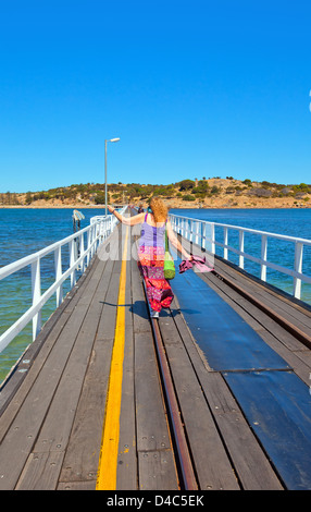 Bunt gekleidete Frau zu Fuß entlang einer Straßenbahn Spur auf dem Damm zwischen Victor Harbor und Granite Island Stockfoto