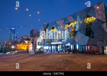 Federation Square bei Nacht mit Flinders Street Station im Hintergrund beleuchtet. Melbourne, Victoria, Australien Stockfoto