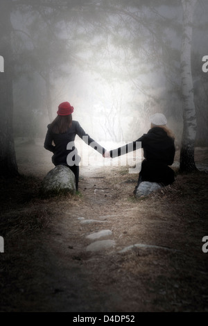 zwei Mädchen sitzen auf Steinen in einem Wald Stockfoto