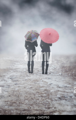 zwei Mädchen mit bunten Sonnenschirmen sind im Nebel wandern. Stockfoto