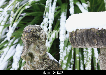 Garten Statue offenbar nach oben auf einen Hügel von Schnee auf eine Vogeltränke aufgetürmt. Schneebedeckte Blätter im Hintergrund. Stockfoto