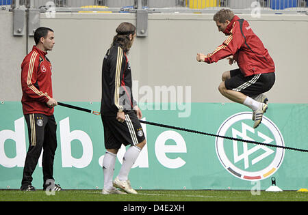 Deutsche Fußball springt internationale Bastian Schweinsteiger (R) über ein Seil, das vom Fitness-Coach Shad Forsythe (L) während einer Trainingseinheit im LTU Arena in Düsseldorf, Deutschland, 8. Oktober 2008 stattfindet. Sein Teamkollege Torsten Frings (C) blickt auf. Die deutsche Nationalmannschaft bereitet sich auf die WM-Qualifikation gegen Russland in Dortmund am 11. Oktober 2008 und gegen Wales in Moenchen Stockfoto