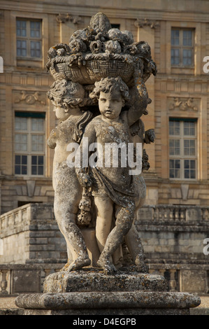 Eine dekorative Statue von cherubic Kleinkinder hält einen Korb mit Blumen und Früchten, in den Gärten des Barock Schloss Vaux-le-Vicomte. Frankreich. Stockfoto