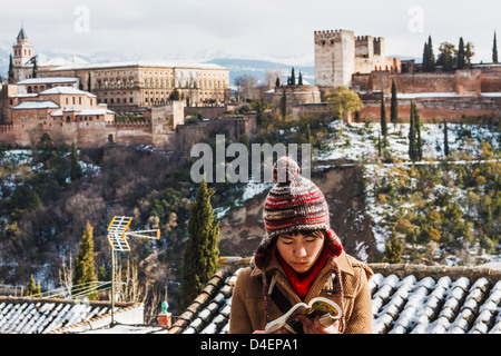 Weibliche japanische Touristen einen Reiseführer mit schneebedeckten Alhambra-Palast im Hintergrund zu lesen. Granada, Spanien Stockfoto