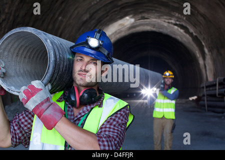 Arbeiter tragen langes Rohr im tunnel Stockfoto