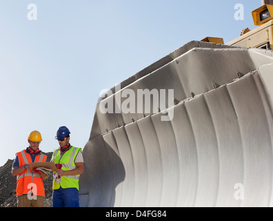 Arbeiter lesen Blaupausen von Digger im Steinbruch Stockfoto