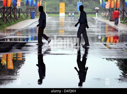 Die Schatten der Beamten überqueren einer Straße in einer Pfütze auf der Olympic Green Tenniszentrum während einer regen Verzögerung in Peking während der Olympischen Spiele 2008 am National Aquatics Center in Peking 10. August 2008 spiegeln sich. Die 1. Vorrundenspiel ist Mens einzigen Tennis-Match von Nicolas Kiefer aus Deutschland und Max Mirnyi aus Belarus unhold wegen starken Regens. Foto: K Stockfoto