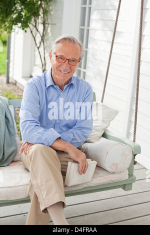 Lächelnder Mann sitzt auf der Veranda-Schaukel Stockfoto