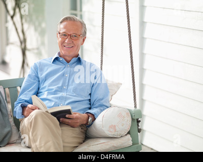 Mann liest Buch über Veranda-Schaukel Stockfoto