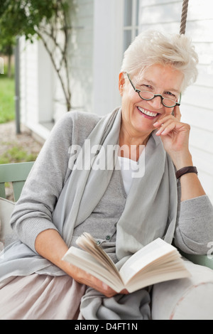 Frau Buch auf der Veranda-Schaukel Stockfoto