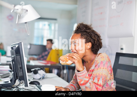 Geschäftsfrau, die Burger am Schreibtisch Essen Stockfoto