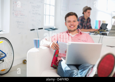 Geschäftsmann mit Laptop auf Sofa im Büro Stockfoto