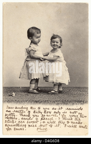Edwardianische Grußkarte mit niedlichen zwei Babys / Kleinkindern, die Hände halten, das Baby auf der linken Seite ist wahrscheinlich ein Junge, der ein Kleid trägt, wie es zu dieser Zeit normal war, geschrieben im Jahr 1904 aus Großbritannien Stockfoto
