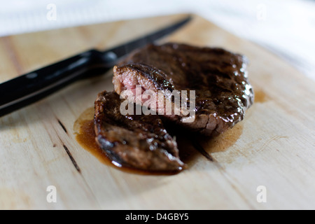 Selten ein Medium Steak, halbieren, mit einem Steak-Messer an der Seite auf einem Holzbrett gegart Stockfoto