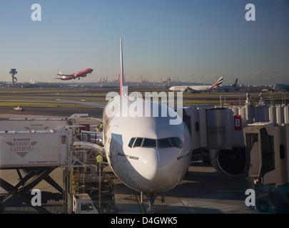 Boeing 777-300 ER Jet Airliner der Emirates Airline am Tor, Emirates und Virgin Blue Flugzeuge hinter Flughafen Sydney, Australien Stockfoto