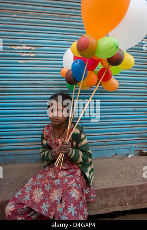 Ein Kind Bettler nimmt eine Pause aus dem Verkauf von Ballons in Mathura, West Uttar Pradesh, Indien Stockfoto
