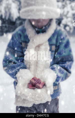 eine Mädchen mit weißen Mütze, Schal und Handschuhe hält ein Weihnachtsgeschenk Stockfoto