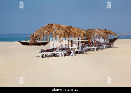 Landschaft mit tropischen Strand-Szene in Goa Indien mit Sonnenanbetern unter Schutz vor der heißen Mitte Tag Sonne auf Liegestühlen chillen Stockfoto