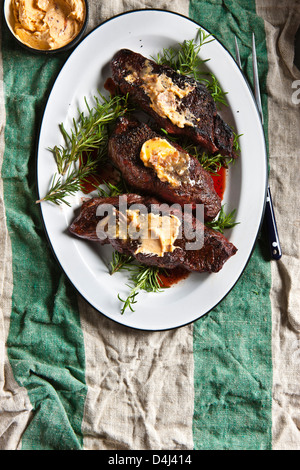 Gegrilltes Steak Denver, garniert mit Sardellen Butter über Rosmarin Zweige auf einem weißen Teller auf einer rustikalen gestreifte Tischdecke. Stockfoto