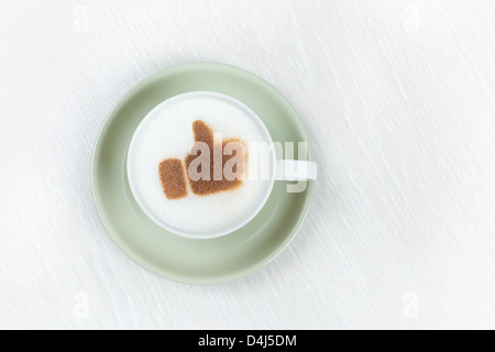 Draufsicht auf eine Tasse gefüllt mit schaumigen Cappuccino mit einem braunen Daumen Schild in Kakaopulver mit Erfolg Stockfoto