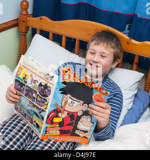 Ein neun Jahre alter Junge liest Beano Comic in seinem Schlafzimmer Stockfoto