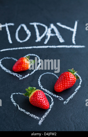 Drei ganze Erdbeeren im inneren Herzen Kreidezeichnungen und heute Wort auf dunklem Hintergrund Stockfoto